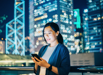 Woman reading emails on smartphone outdoors against financial area of Hong Kong